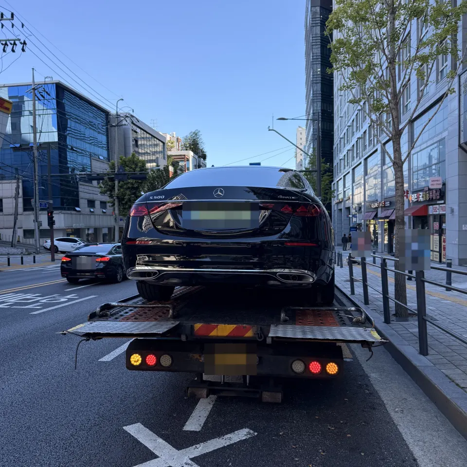 도로에서 탁송 트럭에 실려 이동 중인 검은색 벤츠 S500 세단 후면